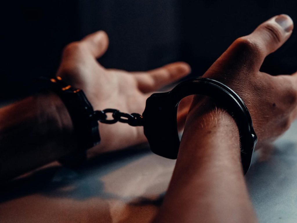 A close-up of human hands handcuffed on a table with a dark background, depicting law enforcement themes.